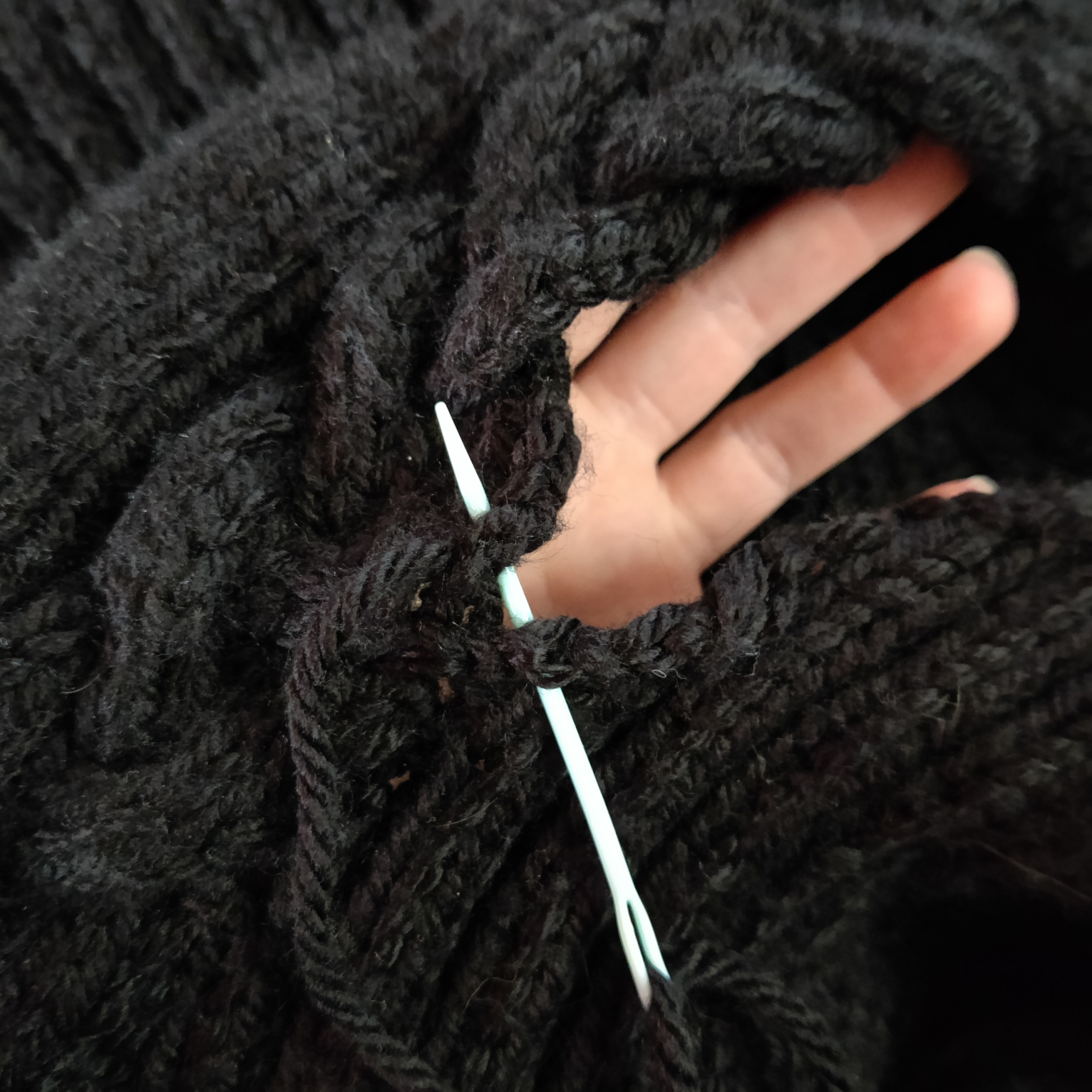 There's an end in sight for the Hopsmere Cardigan pattern! Image of two panels of knitwork being joined with a tapestry needle. There is a hand visible behind the part of the seam still open.